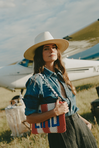Stylish women wearing a stray hat, designer clothing, and purse in front of a private plane