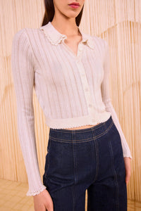 Person wearing a white ribbed blouse with lace details and dark blue jeans against a beige background