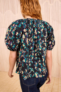 Person wearing a floral blouse with puff sleeves against a beige wall.