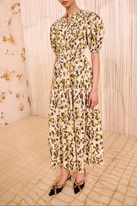 Model wearing a floral dress in a room with floral wallpaper.