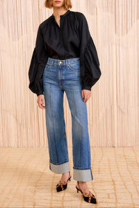 Woman wearing a black blouse and blue jeans against a beige wall.