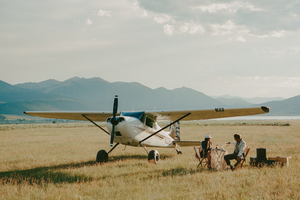 Small airplane on a grassy field with mountains in the background
