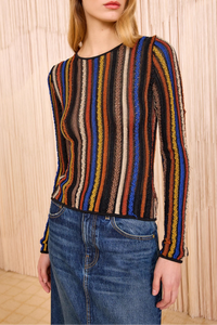Woman wearing a multicolored striped sweater and blue jeans against a wooden paneled wall.