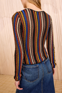 Person wearing a multicolored striped sweater and blue jeans against a wooden paneled wall.